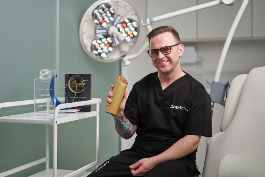 Scalp micropigmentation practitioner seated in clinic setting with treatment equipment